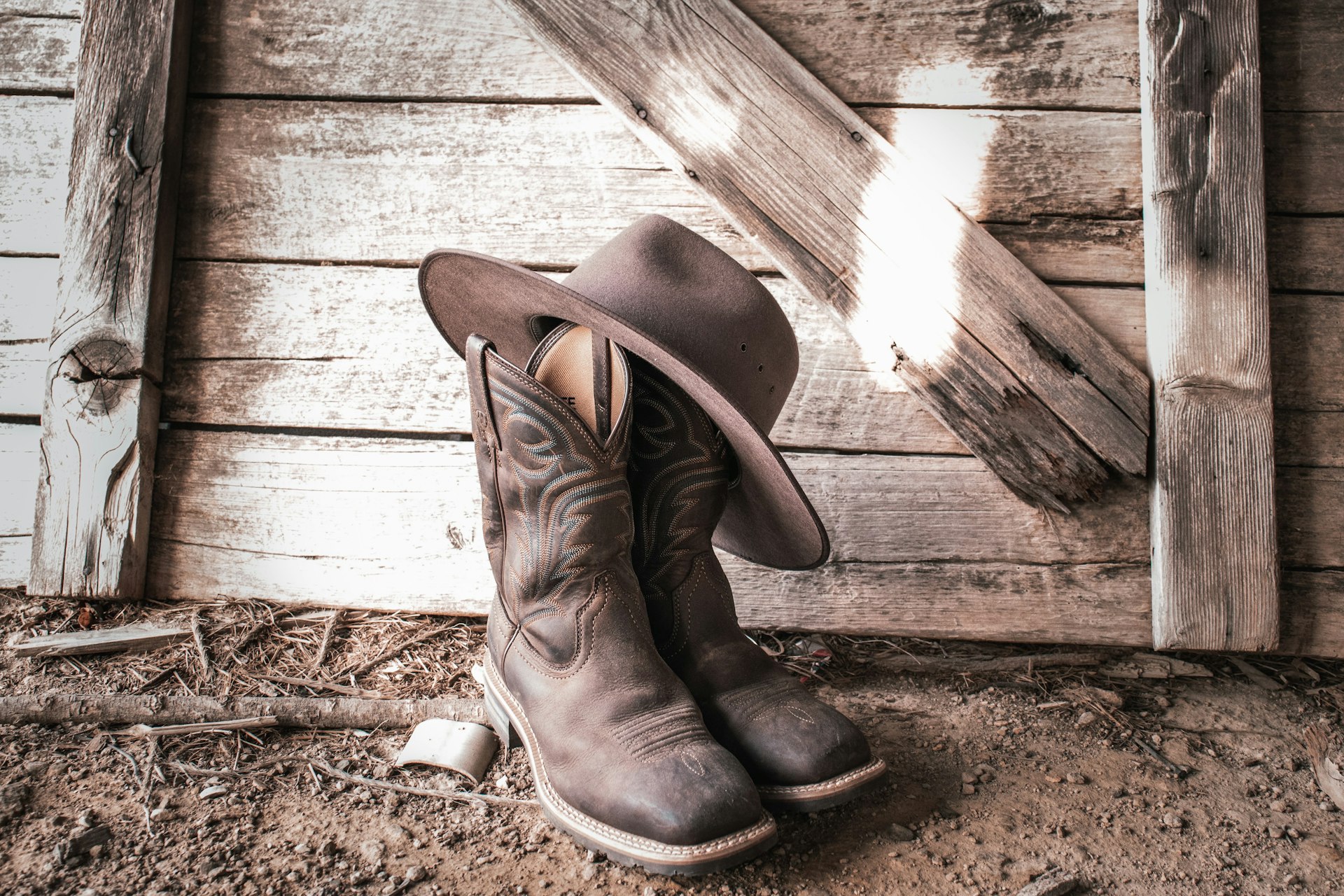 Botas de cuero y sombrero vaquero apoyados en una barda de madera al atardecer